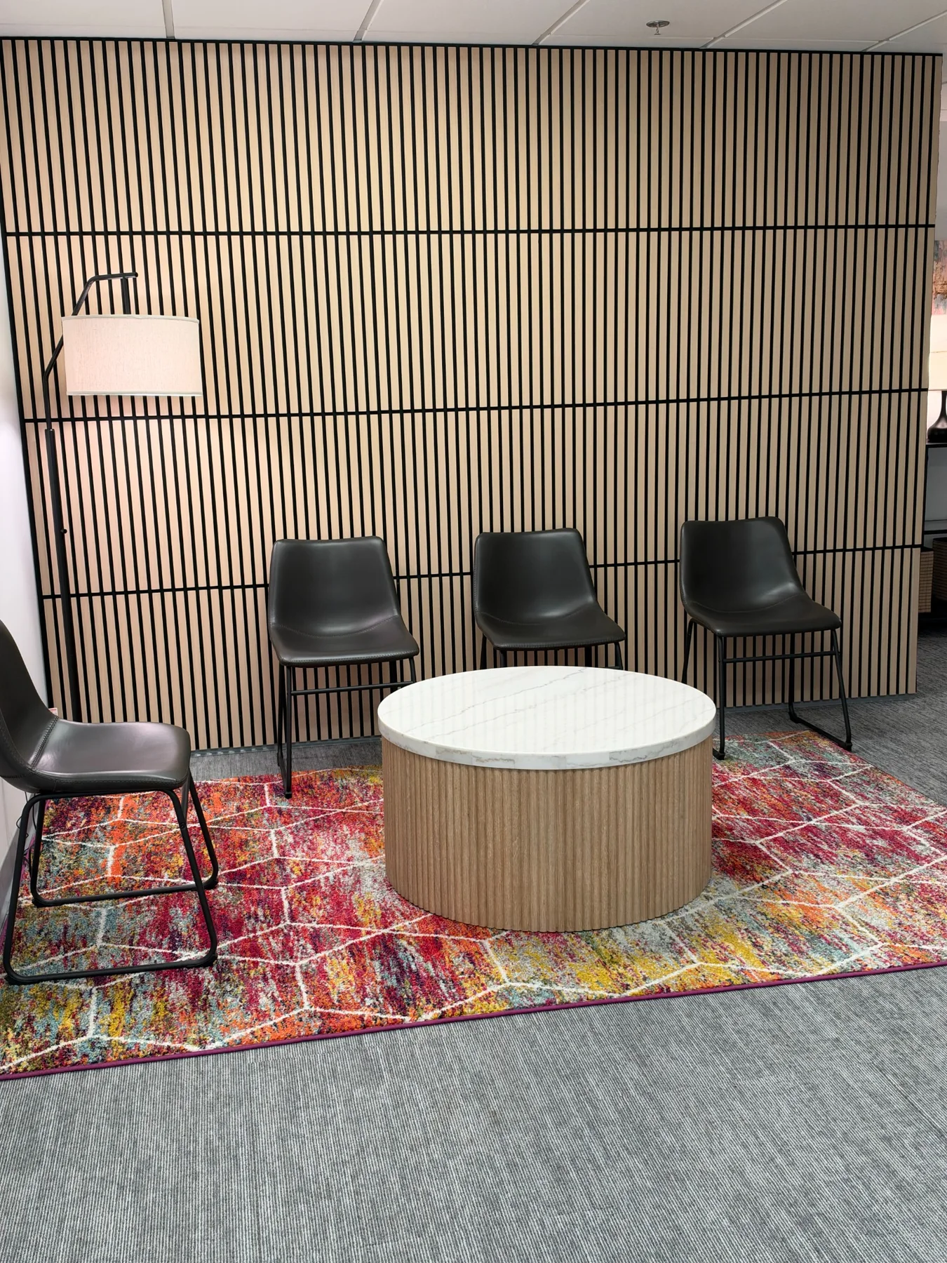 Waiting area with black chairs, a round coffee table, colorful rug, and wood slat feature wall